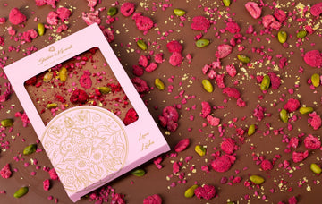 Artisan milk chocolate bar from the Mandala Collection with freeze-dried raspberries, pistachios, and gold leaf, in pink luxury packaging.