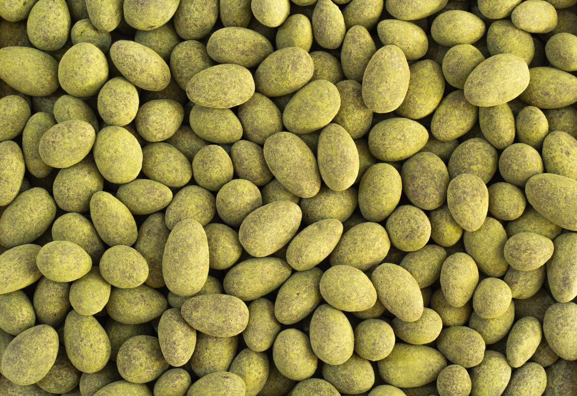 Close-up view of green, moringa‑coated dark chocolate almonds clustered together.
