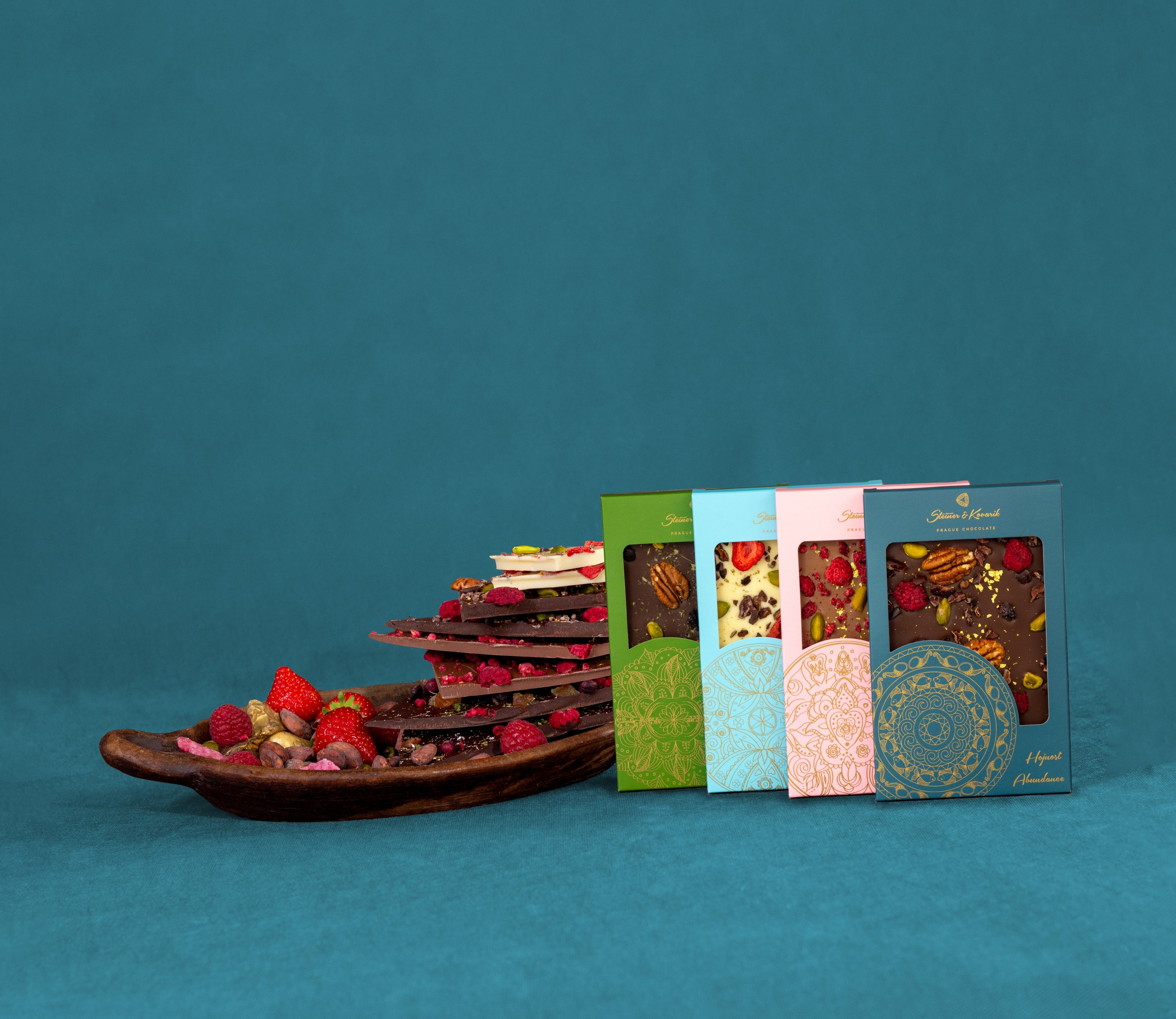 Premium handcrafted European chocolate bars with dried fruit and nuts in elegant Steiner & Kovarik mandala gift packaging, displayed beside artisanal chocolate bark topped with strawberries and raspberries.