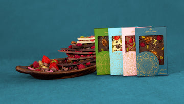 Luxury artisan chocolate bars with fruit and nut toppings in colorful mandala gift packaging by Steiner & Kovarik, displayed beside gourmet chocolate bark layered with strawberries and raspberries.